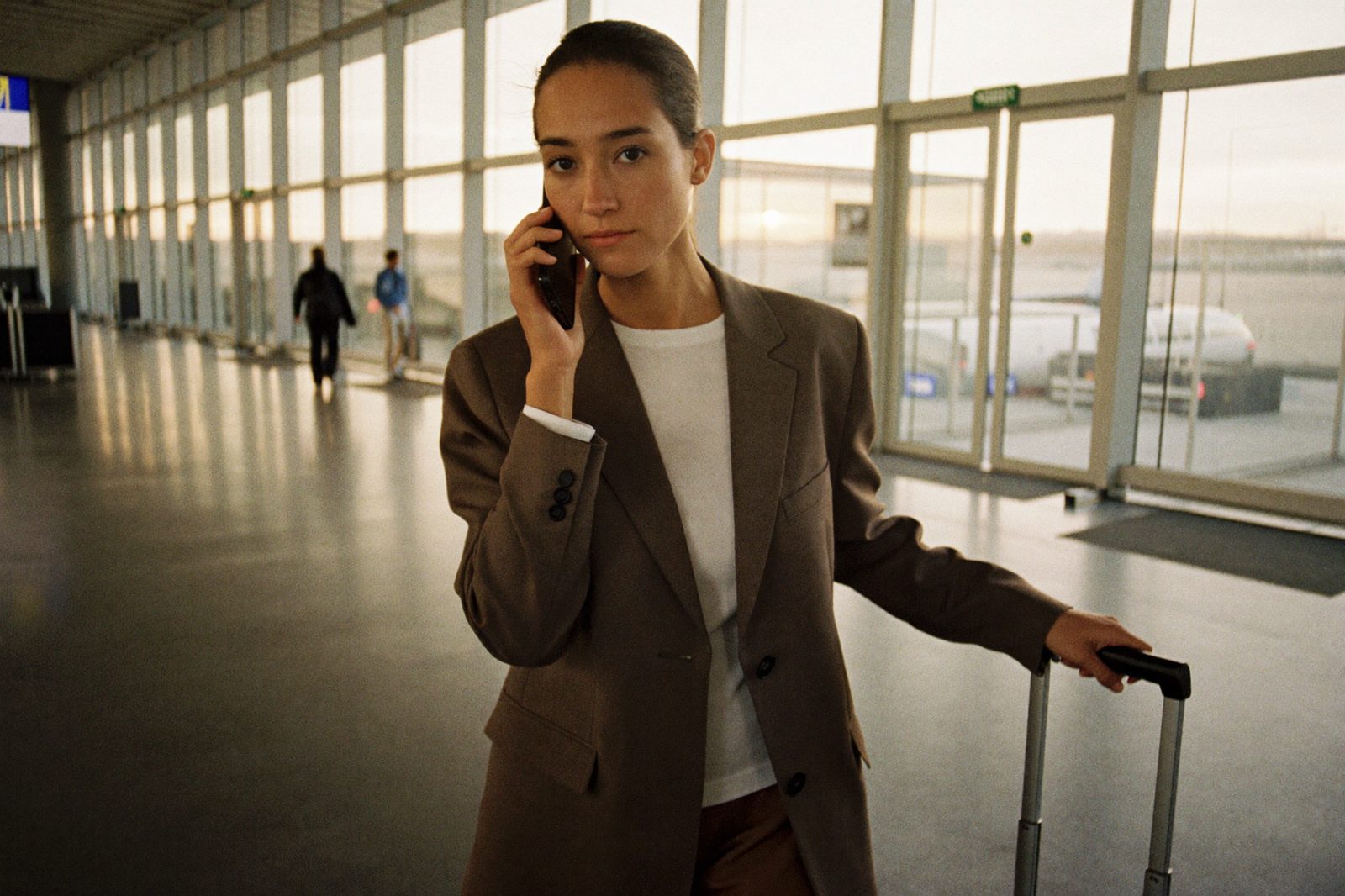 A businesswoman taking a call in the terminal at dawn, carry-on at her side - her number, still reachable
