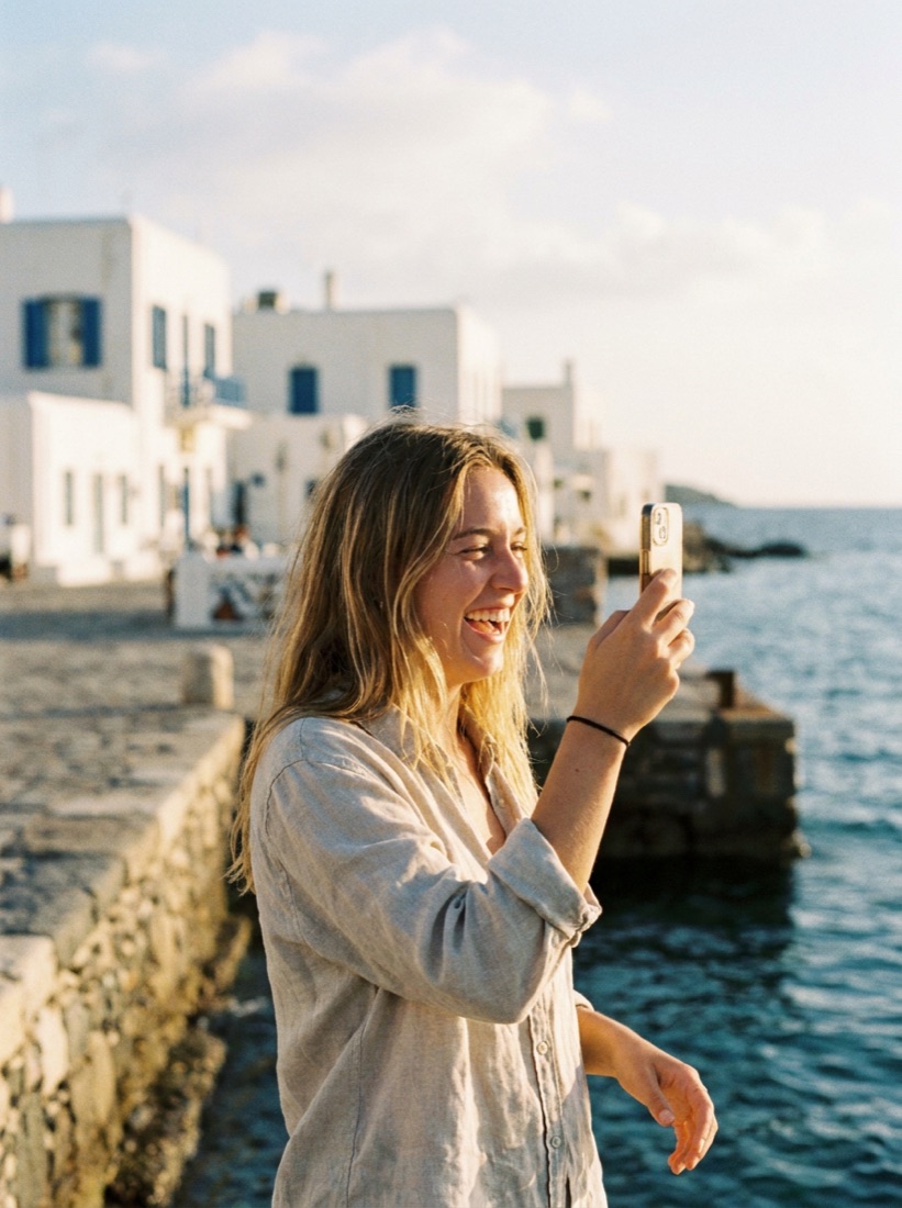 A traveler alone on a Greek harbour, sharing a moment by phone